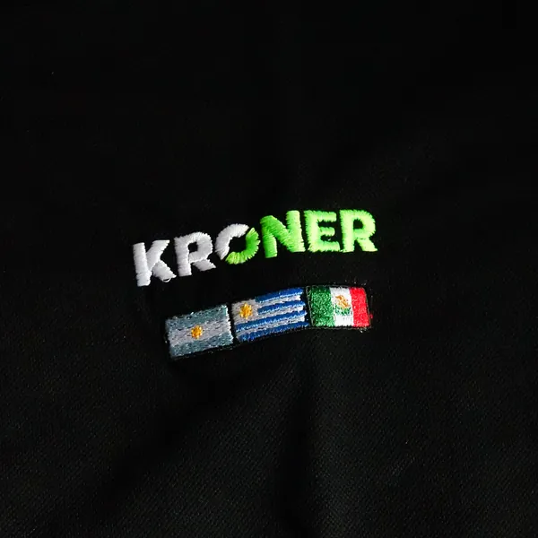 Chomba negra con logo Kroner y banderas bordadas en el pecho